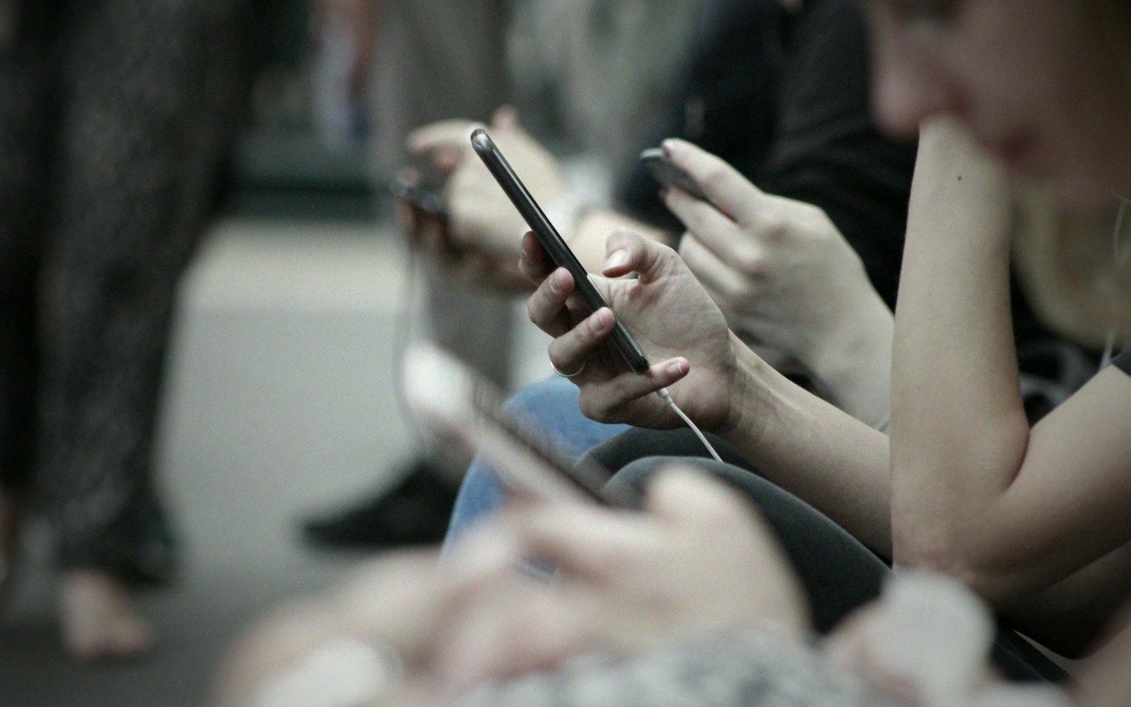 Todo mundo no celular: fileira de pessoas lado a lado, cada uma na própria tela.